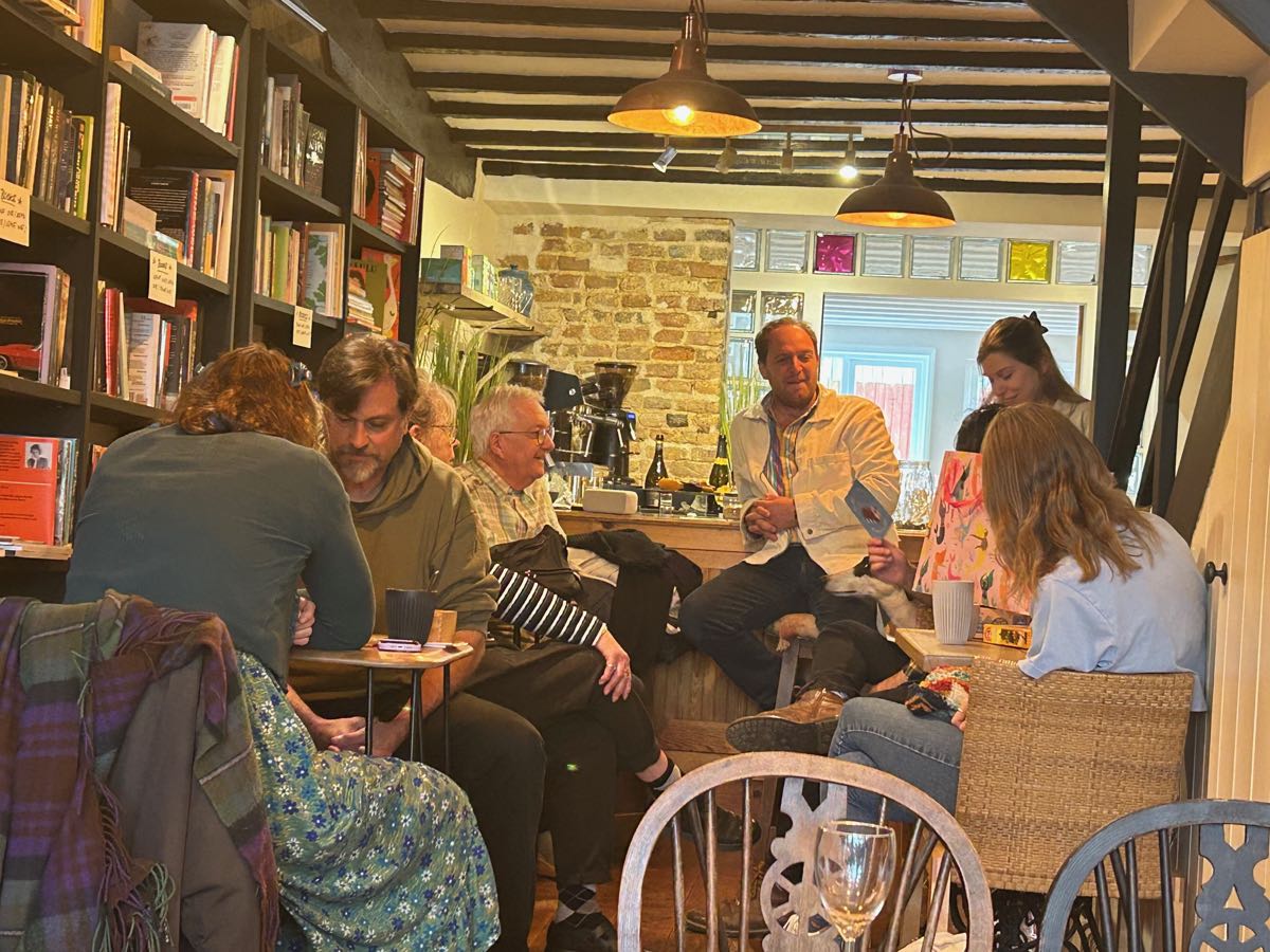 Inside the cafe: exposed beams and brick, shelves of books, and people sitting talking over drinks.